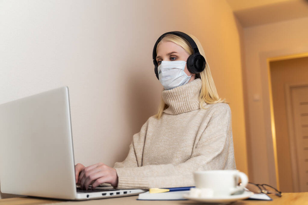 Girl in a protective mask and headphones is typing on a laptop - Foto, Imagem
