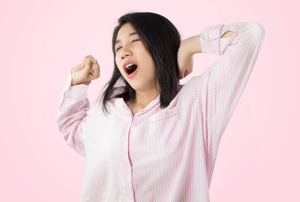 young asian woman wear pink pajamas yawn and stretch when her wake up feeling sleepy - Photo, Image