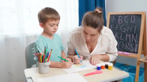 Piccolo bambino con giovane madre disegno e pittura con matite colorate. Fare i compiti e l'edcucation con i genitori. - Filmati, video
