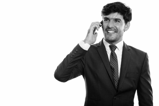 Przemyślany młody, szczęśliwy perski biznesmen uśmiecha się rozmawiając przez telefon komórkowy i patrząc w górę - Zdjęcie, obraz