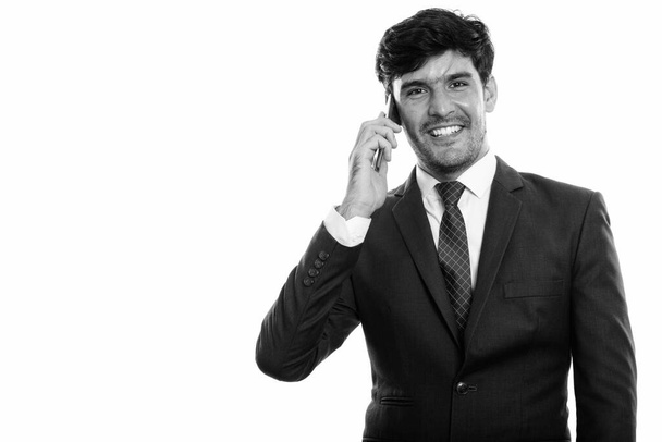 Studio zdjęcie młodego szczęśliwego perskiego biznesmena uśmiechającego się podczas rozmowy przez telefon komórkowy - Zdjęcie, obraz