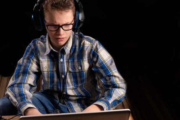 Niño con camisa y gafas haciendo la tarea en el portátil con auriculares - Foto, Imagen