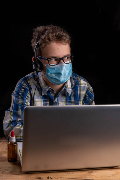 Menino com óculos e camisa e máscara bucal com fone de ouvido e laptop com espaço livre de texto - Foto, Imagem