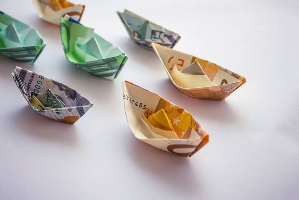 Banknotes rolled up in the form of ships. Revenues and expenses of shipping and cruise companies. Light background, vignetting. - Photo, Image
