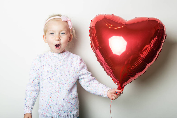 Surprised little girl holding a heart air balloon on a light background. Concept for Valentine's Day, birthday. Banner. - Photo, Image