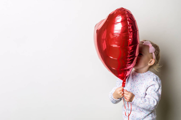 Little girl holding a heart air balloon on a light background. Concept for Valentine's Day, birthday. Banner. - Foto, immagini
