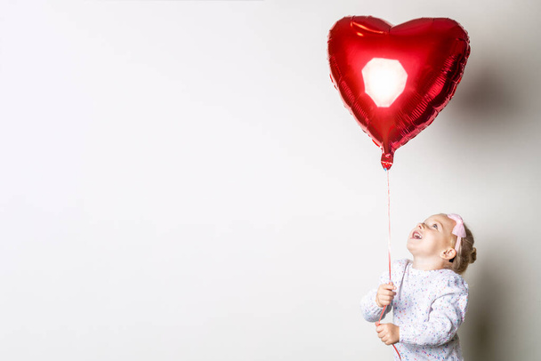 Little girl catches a heart air balloon on a light background. Concept for Valentine's Day, birthday. Banner. - Foto, imagen