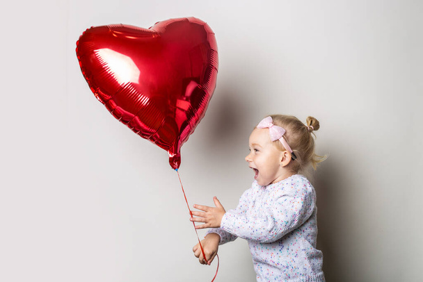 Little girl catches a heart air balloon on a light background. Concept for Valentine's Day, birthday. Banner. - Foto, Imagen