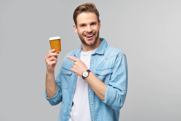 Portrait of young handsome caucasian man in jeans shirt over light background holding cup of coffee to go - Fotó, kép