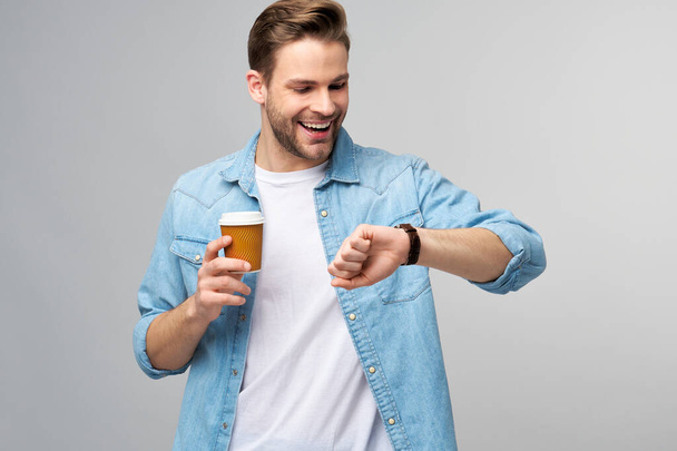 Portrait of young handsome caucasian man in jeans shirt over light background holding cup of coffee to go - Foto, imagen