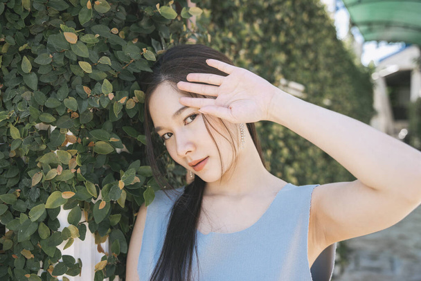 Портрет молодой азиатской красавицы в голубой рубашке у стены зеленого листа. - Фото, изображение