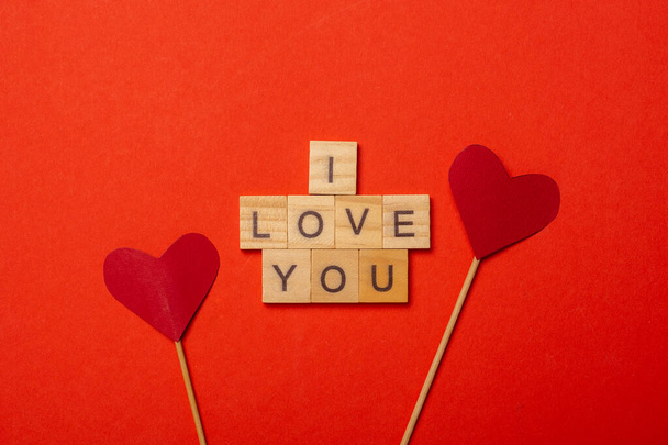 Plaques en bois avec le texte Je t'aime et les coeurs sur des bâtons sur un fond rouge. Composition Saint Valentin. Bannière. Couché plat, vue du dessus. - Photo, image
