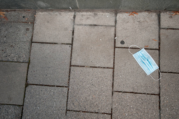 Eine hellblaue Mund- und Nasenmaske liegt auf dem Bürgersteig. - Foto, Bild