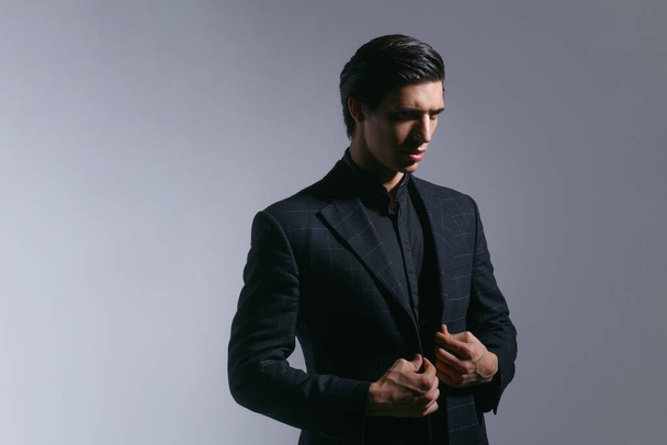 Portrait of handsome young man in black stylish suit, over on dark grey background. - Foto, Imagen