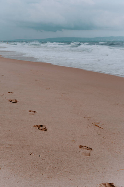 Fußabdrücke im Sand. Strand, Welle und Fußabdrücke auf einem Sandstrand. Meer, Sand. Bewölkter Himmel. - Foto, Bild