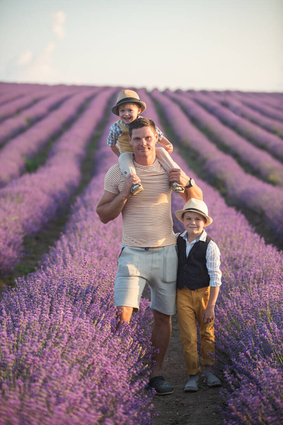 Stylishly dressed boys in straw hats and plaid shirts. Dad and his sons are walking. A huge blooming lavender field. Family on a walk - Foto, afbeelding