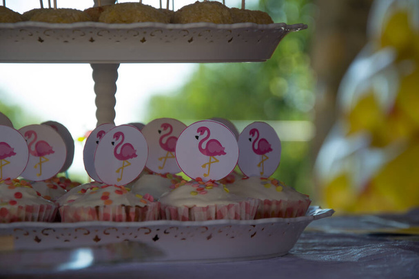 Close-up of homemade cupcakes with pink flamingo sticks decoration on cake-stand, party concept, sweets for birthday celebration - Photo, Image