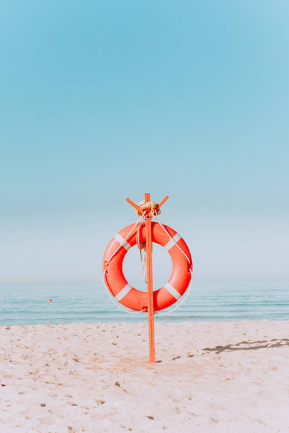 bouée de sauvetage rouge sur une plage de sable aux couleurs pastel. Bouée de sauvetage rouge sur le rivage sablonneux de la plage par une journée ensoleillée. - Photo, image