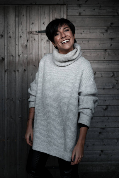 Ritratto di bellezza di una donna alla moda davanti a un muro di legno che indossa abiti invernali mentre guarda la macchina fotografica con un sorriso perfetto - Foto, immagini