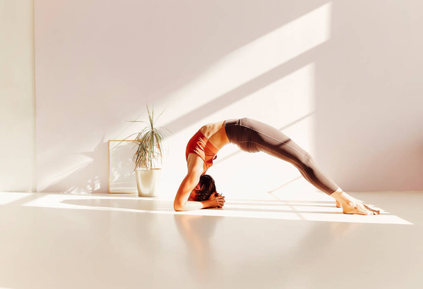 Vista lateral de la tranquila hembra en ropa deportiva practicando yoga en pose de luciérnaga mientras se equilibra en los brazos sobre la esterilla y mirando hacia otro lado - Foto, imagen