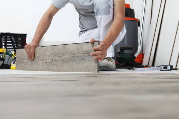 木材積層ビニール床を設置する労働者の手。木造家屋改修. - 写真・画像