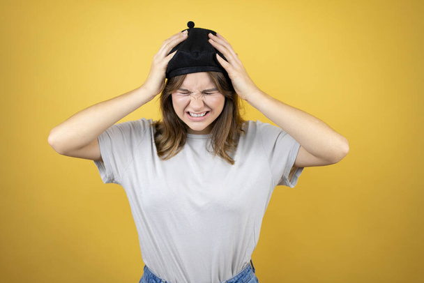 Beautiful young caucasian girl wearing french look with beret over isolated yellow background suffering from headache desperate and stressed because pain and migraine with her hands on head - Fotografie, Obrázek