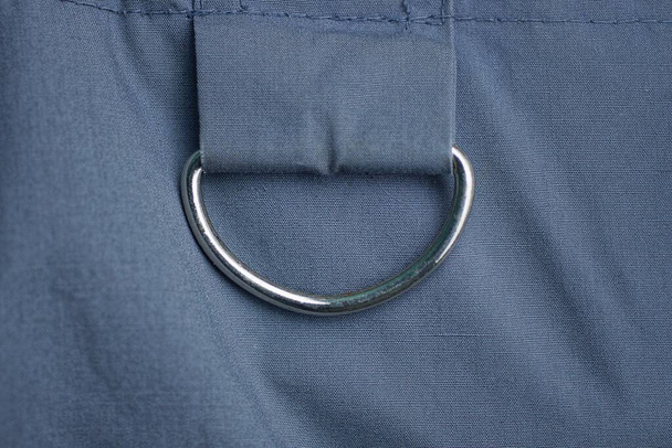 un anillo de metal blanco en un arnés sobre una tela gris de una prenda de vestir - Foto, imagen