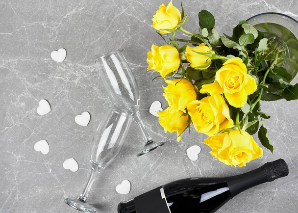 Rose gialle, bottiglia di spumante, champagne flauto e cuori bianchi su sfondo grigio.Regalo, vacanza, Incontri. San Valentino, Festa della mamma, Festa della donna - Foto, immagini