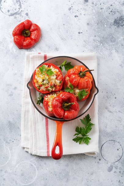Red bell peppers stuffed with rice and vegetables on cast iron pan on gray concret background. - 写真・画像