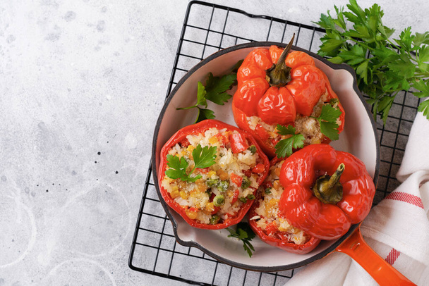 Red bell peppers stuffed with rice and vegetables on cast iron pan on gray concret background. - Foto, Imagen