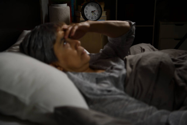 Depressziós idős nő fekszik az ágyban nem tud aludni az álmatlanságtól. Az ébresztőórára való szelektív összpontosítás - Fotó, kép