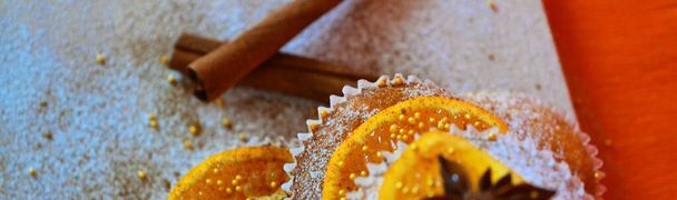 Torre de magdalenas decorada con azúcar en polvo, rodajas de mandarina, bolitas de azúcar dorada y anís estrellado sobre fondo naranja - Foto, Imagen