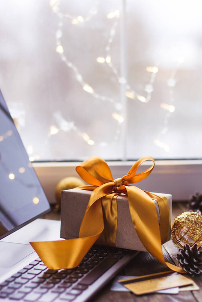 Gift with a gold ribbon and a laptop and Bank card on a wooden table Christmas online shopping - 写真・画像