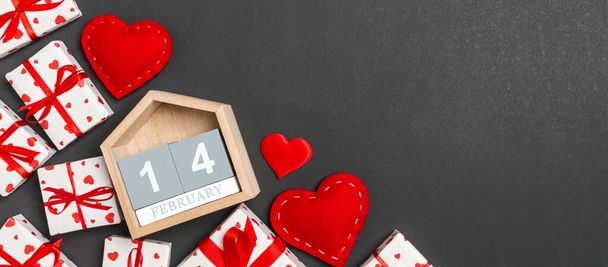 Κάτοψη των κιβωτίων δώρων, ξύλινο ημερολόγιο και κόκκινο ύφασμα καρδιές σε πολύχρωμο φόντο. Στις 14 Φεβρουαρίου του τρέχοντος έτους. Αγίου Βαλεντίνου έννοια με αντίγραφο χώρο. - Φωτογραφία, εικόνα