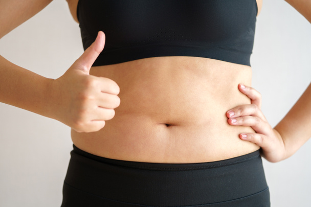 Γυναίκες με χοντρή κοιλιά. παχύσαρκο χέρι γυναίκας κρατώντας υπερβολικό λίπος στην κοιλιά. δίαιτα έννοια τρόπο ζωής για να μειώσει την κοιλιά και να διαμορφώσει υγιή μυϊκό ιστό του στομάχου. - Φωτογραφία, εικόνα