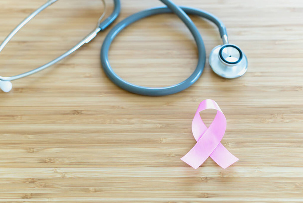 Pink ribbon and stethoscope on wooden table. Symbol of breast cancer, health care concept. Cancer day - Фото, зображення