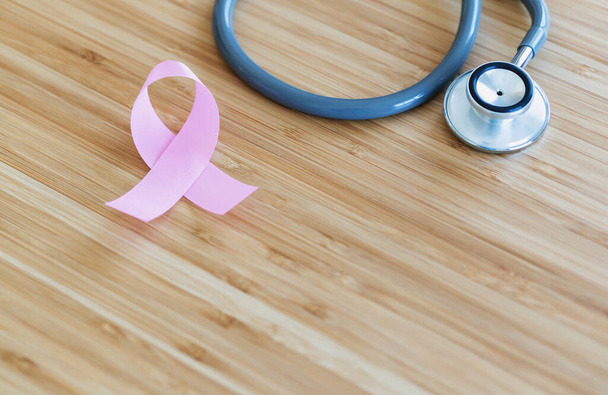 Pink ribbon and stethoscope on wooden background, closeup. Breast cancer awareness concept - Foto, Imagem