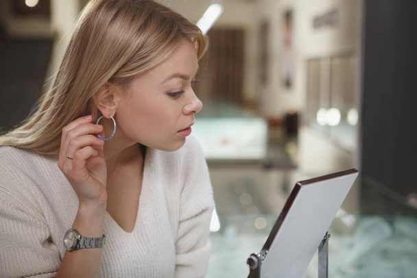 close-up van een prachtig vrouw proberen op diamant oorbellen bij sieraden winkel - Foto, afbeelding