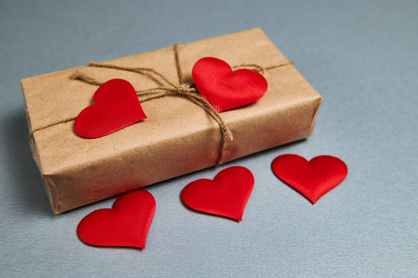Caja de regalo de San Valentín envuelta en papel artesanal y corazones rojos sobre un fondo gris - Foto, Imagen