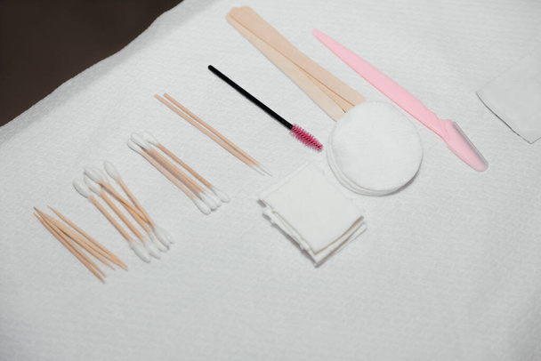 Sterile napkins, cotton pads, wooden sticks, pink brush, buds. Beautician tools for making eyebrows makeup. Facial care and make up in a professional beauty salon.  - Foto, Imagem