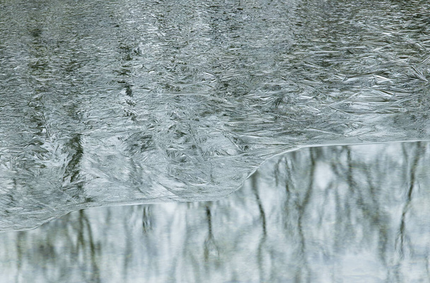Primer plano de invierno de un patrón de hielo plateado abstracto y con reflejos de árboles en aguas tranquilas, Eagle Lake, Fort Custer State Park, Michigan, EE.UU. - Foto, Imagen