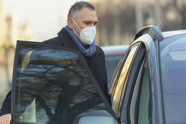 Ώριμος άνδρας που φοράει μάσκα προσώπου κατά τη διάρκεια της πανδημίας covid-19 μπαίνει σε ένα αυτοκίνητο - Φωτογραφία, εικόνα
