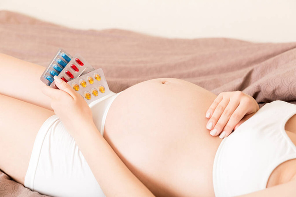 Intersection de la femme enceinte prenant des pilules vitaminiques sur le canapé à la maison. - Photo, image