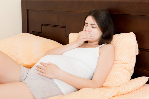 Pregnant suffering with nausea. Pregnancy symptoms, expectation toxicosis. Young vomiting woman sitting on bed. parenthood concept. - Foto, Imagem