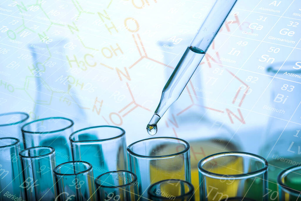 Het laten vallen van chemische vloeistof om buis te testen met laboratorium glaswerk achtergrond. Onderzoek- en ontwikkelingsconcept voor wetenschap of chemie.  - Foto, afbeelding