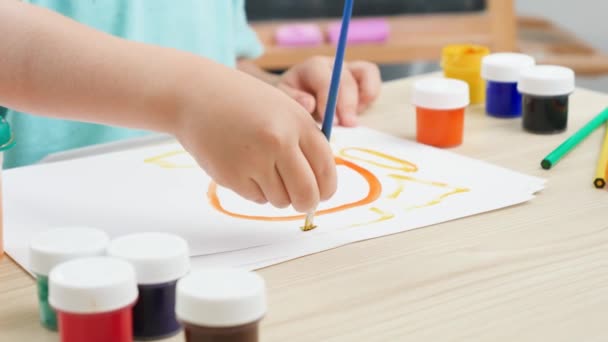 Niño sentado detrás del escritorio y dibujando un cuadro colorido con pintura y pinceles. Educación infantil en el hogar durante el autoaislamiento y el encierro. Concepto de arte y creatividad de los niños - Imágenes, Vídeo