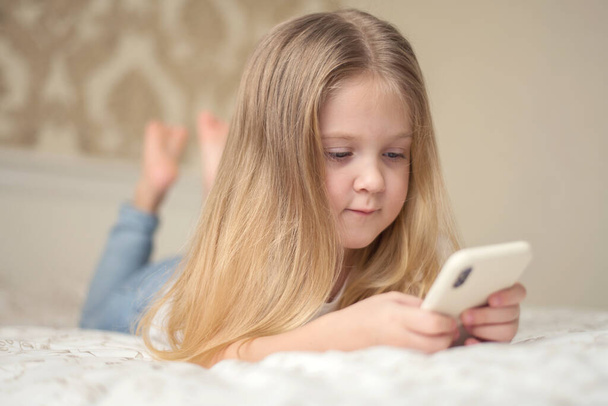 Little girl in bed playing a tablet in social internet. Close up of little girl watching video on the digital tablet - Foto, Imagen