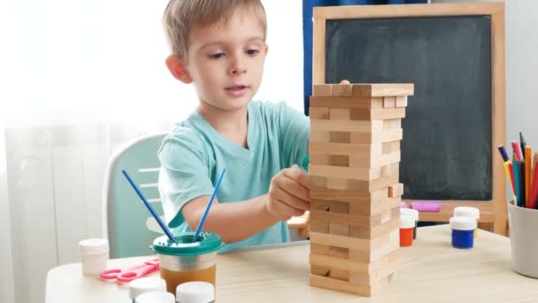 Niño inteligente sacando bloques de madera de la torre alta hecha de ladrillos. Concepto de niños inteligentes y educación en el hogar durante el encierro y el autoaislamiento. - Metraje, vídeo