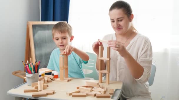Genç anne küçük oğluyla oynuyor ve oturma odasındaki tahta bloklardan ve tuğlalardan kule inşa ediyor. Tecrit ve tecrit süresince akıllı çocuklar ve evde eğitim kavramı - Video, Çekim