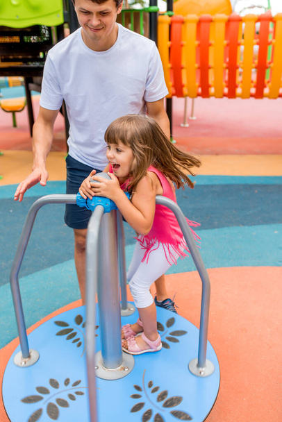 man dad plays with daughter, girl 5-6 years old, summer city on sports playground. Emotion of joy, fun, relaxation delight carousel. Concept of happy family, daddy day. Caring for raising children. - Foto, Imagem